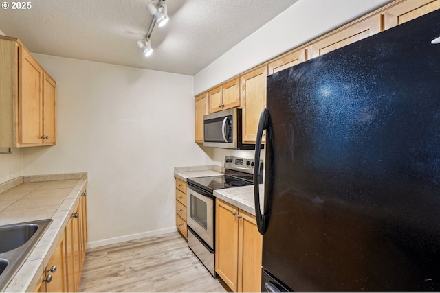 kitchen with tile countertops, light hardwood / wood-style floors, stainless steel appliances, light brown cabinets, and a textured ceiling