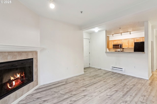 unfurnished living room with a tiled fireplace, a baseboard radiator, track lighting, and light hardwood / wood-style flooring