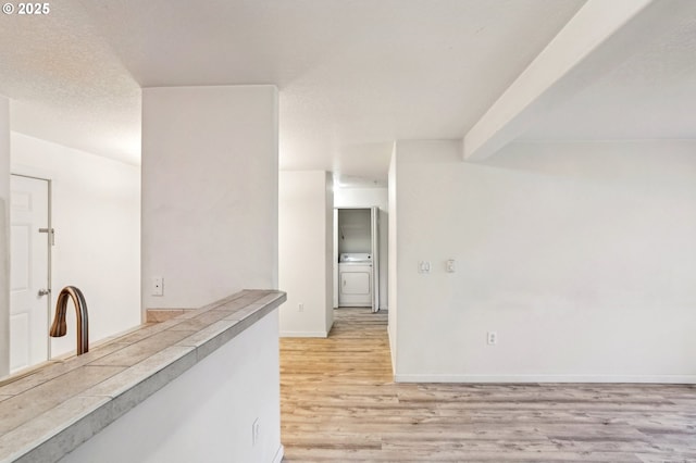 interior space with beamed ceiling, washer / dryer, a textured ceiling, and light wood-type flooring