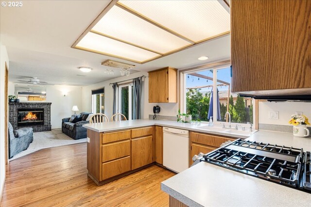 kitchen with a sink, dishwasher, light countertops, a peninsula, and open floor plan