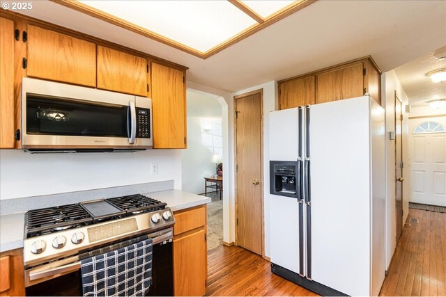 kitchen with light countertops, appliances with stainless steel finishes, arched walkways, and hardwood / wood-style flooring
