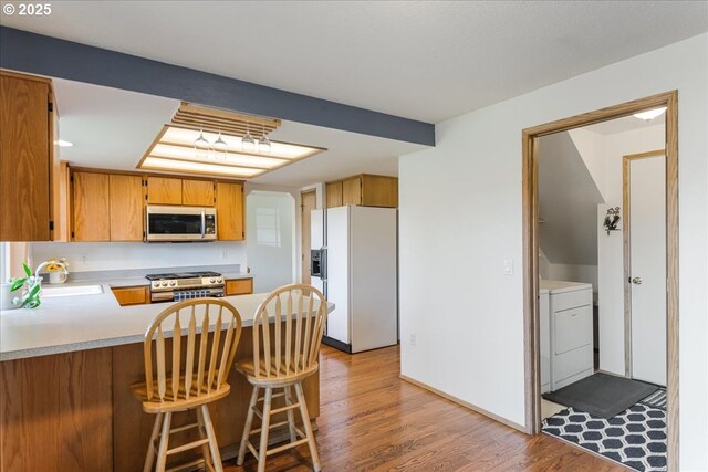 kitchen with appliances with stainless steel finishes, a sink, light wood finished floors, light countertops, and washing machine and dryer