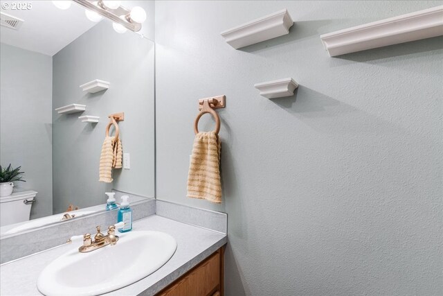 half bathroom with vanity, toilet, and visible vents