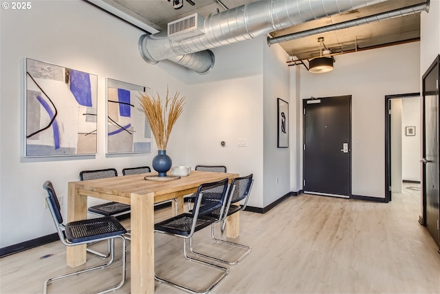 dining space featuring baseboards, visible vents, a high ceiling, and light wood-style floors