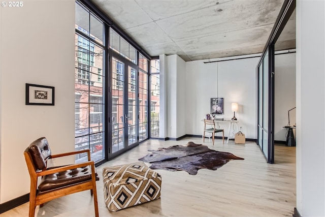 living area with a high ceiling, baseboards, expansive windows, and light wood-style flooring