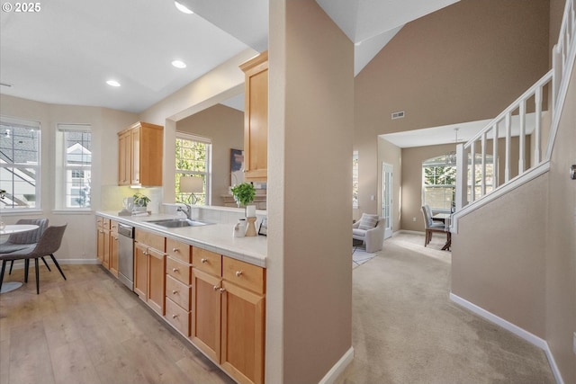 kitchen featuring vaulted ceiling, dishwasher, sink, light carpet, and light brown cabinetry