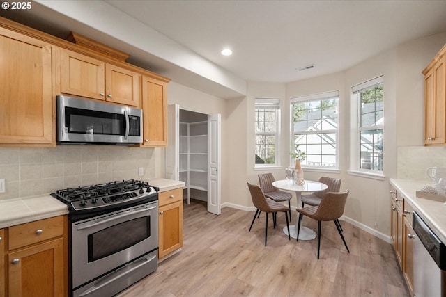 kitchen with light brown cabinets, appliances with stainless steel finishes, light hardwood / wood-style floors, and tasteful backsplash