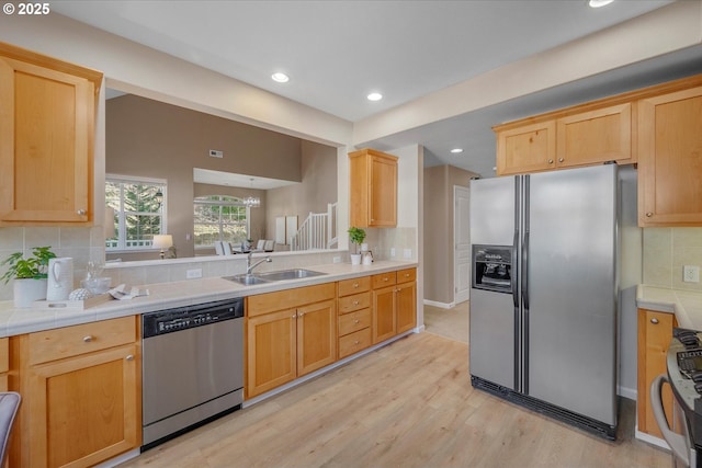 kitchen featuring stainless steel appliances, an inviting chandelier, decorative backsplash, sink, and light hardwood / wood-style flooring