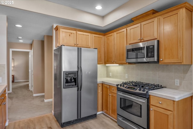 kitchen with tasteful backsplash, appliances with stainless steel finishes, tile countertops, and light hardwood / wood-style floors