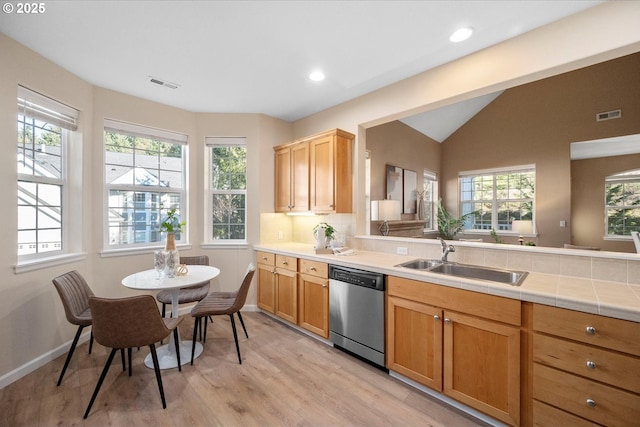 kitchen featuring vaulted ceiling, tile countertops, stainless steel dishwasher, sink, and light wood-type flooring