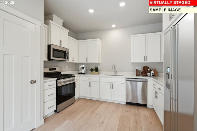 kitchen with stainless steel appliances, white cabinetry, sink, and light hardwood / wood-style floors