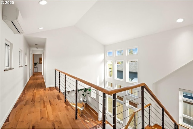 hallway featuring an upstairs landing, a wall mounted AC, wood finished floors, and lofted ceiling