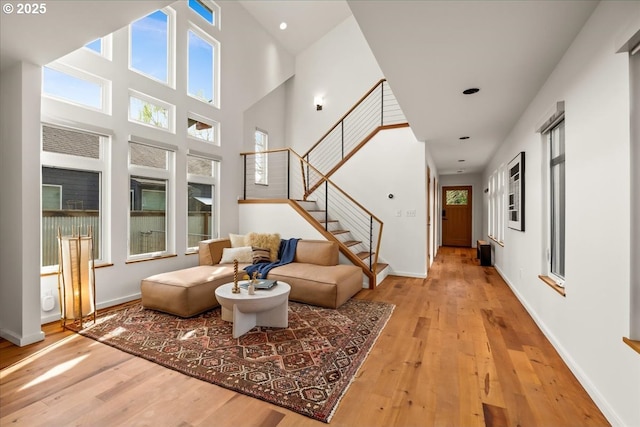 living area featuring baseboards, light wood finished floors, a towering ceiling, and stairs