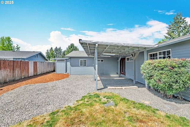 back of house with an attached carport, gravel driveway, fence, an outdoor structure, and a storage unit