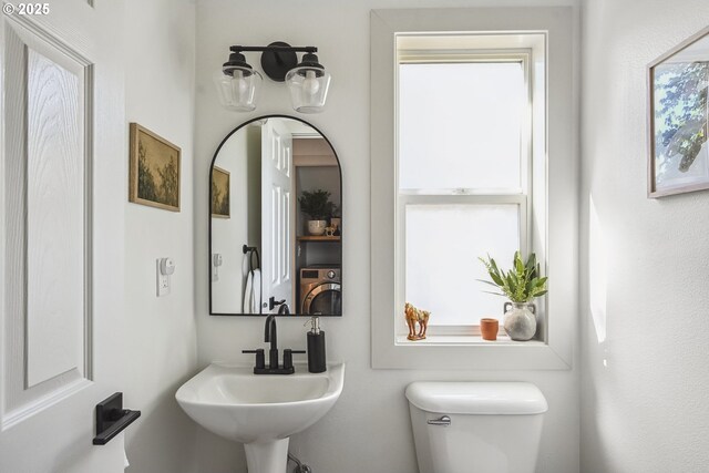 half bathroom with toilet, washer / clothes dryer, and a sink