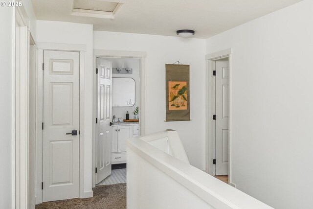 hall with light carpet, a sink, an upstairs landing, and attic access