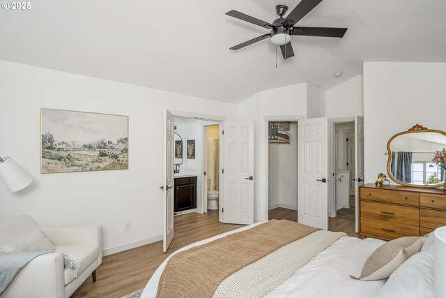 bedroom featuring vaulted ceiling, light wood finished floors, a walk in closet, ensuite bath, and baseboards