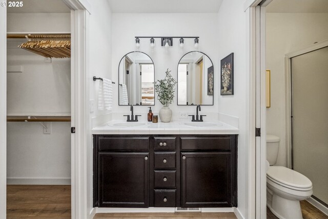 full bath featuring toilet, double vanity, wood finished floors, baseboards, and a walk in closet