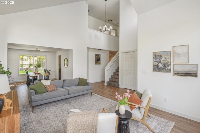 living area featuring stairway, wood finished floors, a chandelier, baseboards, and a towering ceiling