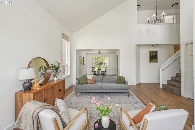 living room with a chandelier, high vaulted ceiling, wood finished floors, stairway, and baseboards
