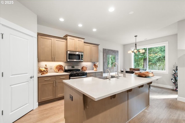 kitchen with decorative backsplash, light wood-style flooring, appliances with stainless steel finishes, and a kitchen island with sink