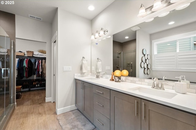 full bath featuring visible vents, double vanity, a stall shower, wood finished floors, and a sink