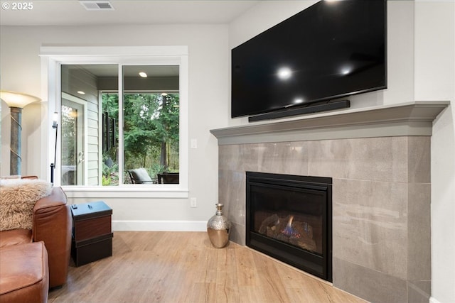 living area with visible vents, wood finished floors, baseboards, and a tile fireplace