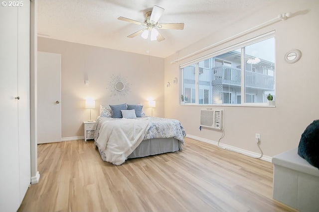 bedroom featuring an AC wall unit, light hardwood / wood-style flooring, ceiling fan, and a textured ceiling