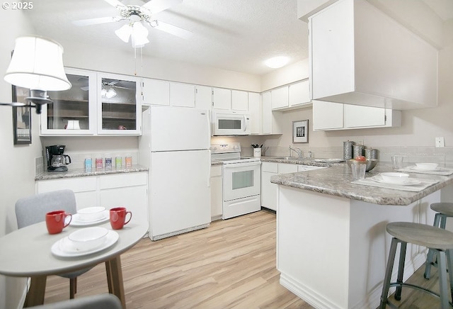 kitchen with white appliances, sink, light hardwood / wood-style floors, kitchen peninsula, and white cabinets