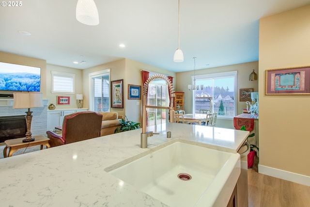 kitchen featuring light hardwood / wood-style floors, light stone countertops, pendant lighting, a fireplace, and sink