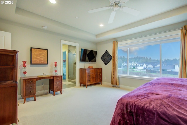 bedroom with a raised ceiling, connected bathroom, ceiling fan, and light colored carpet