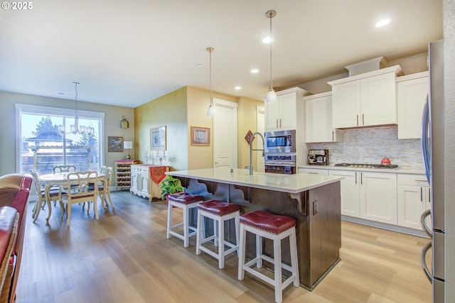 kitchen featuring stainless steel appliances, white cabinets, a kitchen island with sink, and pendant lighting