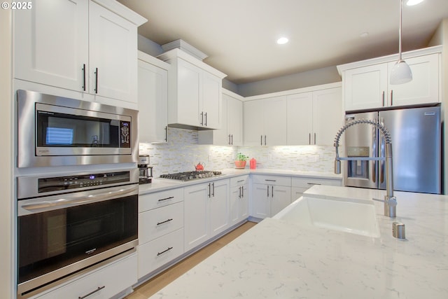 kitchen featuring decorative light fixtures, appliances with stainless steel finishes, white cabinetry, and sink