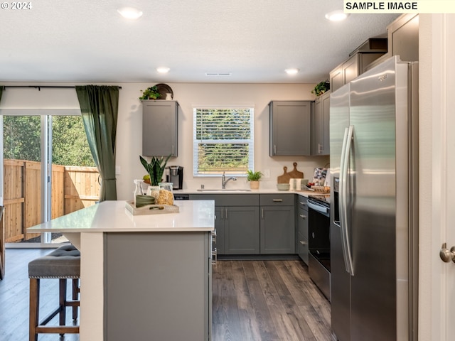 kitchen with a kitchen island, a sink, light countertops, appliances with stainless steel finishes, and gray cabinets