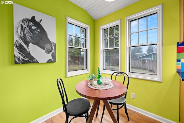 dining room featuring lofted ceiling, light wood-style flooring, and baseboards