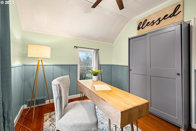 home office featuring a wainscoted wall, lofted ceiling, visible vents, ceiling fan, and wood finished floors