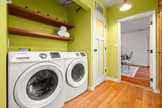 clothes washing area with visible vents, light wood-style flooring, washing machine and dryer, laundry area, and baseboards