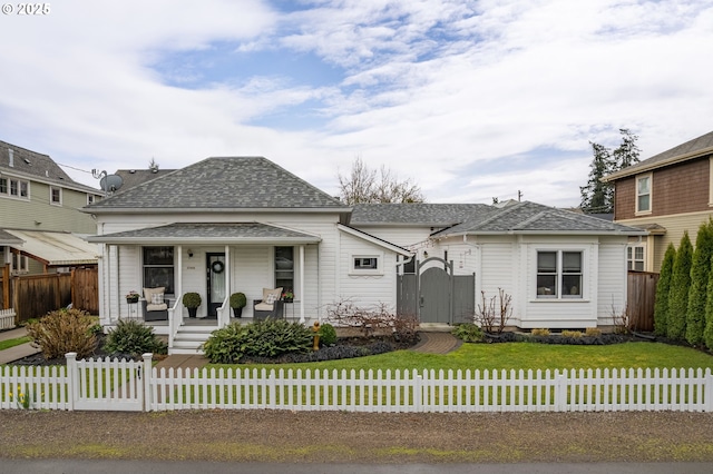 bungalow-style house with a fenced front yard, covered porch, a shingled roof, and a gate