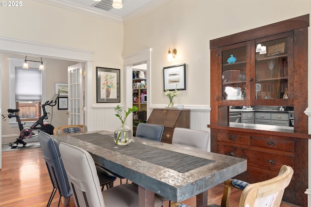 dining room with visible vents, light wood-type flooring, a wainscoted wall, and ornamental molding