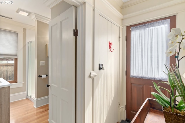 hallway with visible vents, light wood-style flooring, crown molding, and baseboards