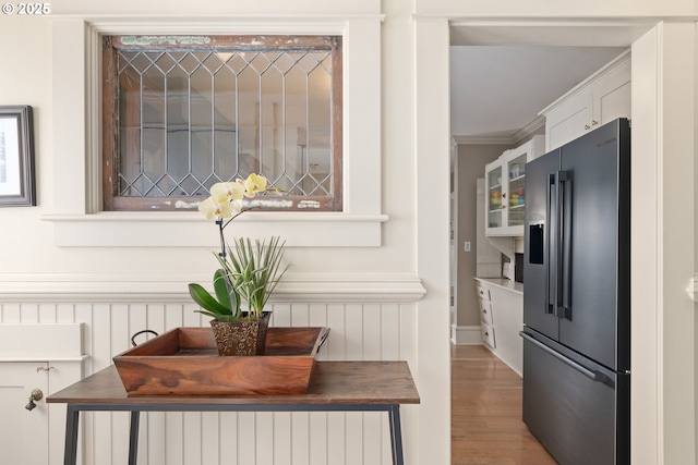 details with a wainscoted wall, ornamental molding, white cabinetry, stainless steel fridge, and butcher block counters