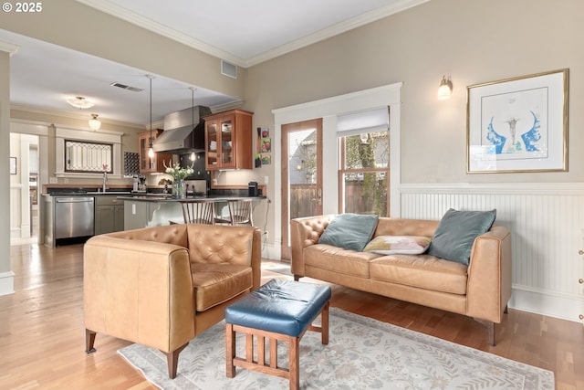 living area with visible vents, ornamental molding, and light wood-style flooring