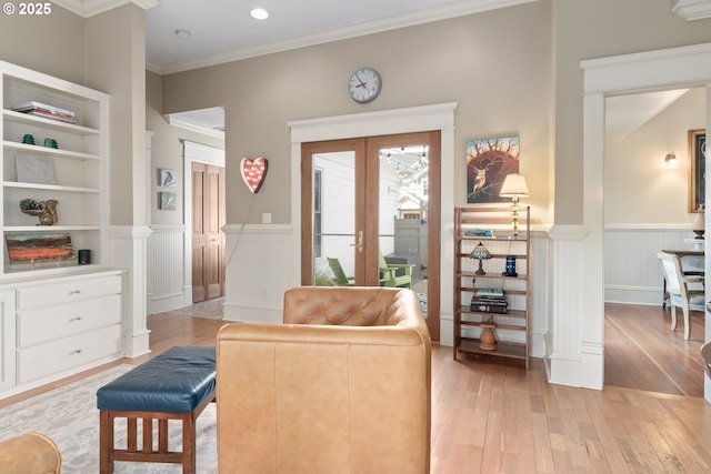 living area with crown molding, light wood-style floors, a wainscoted wall, and french doors