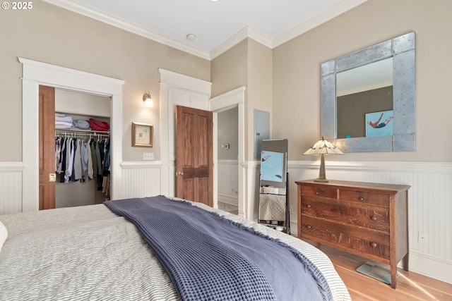 bedroom with a walk in closet, ornamental molding, wainscoting, wood finished floors, and a closet