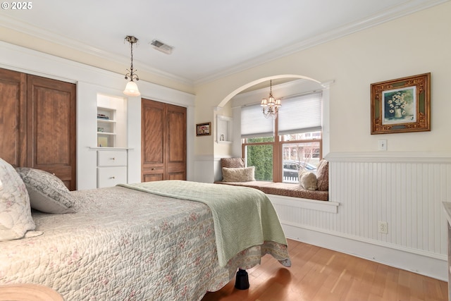 bedroom with wood finished floors, visible vents, arched walkways, ornamental molding, and wainscoting