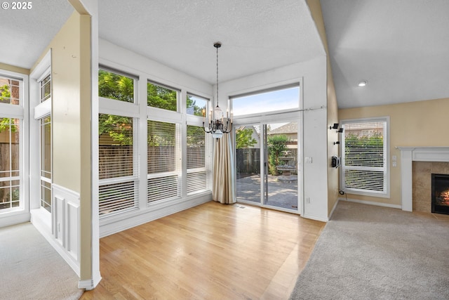unfurnished dining area featuring a chandelier, a fireplace, baseboards, wood finished floors, and a textured ceiling