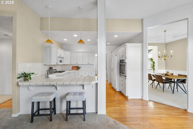 kitchen featuring white appliances, tile countertops, a peninsula, a sink, and a kitchen bar