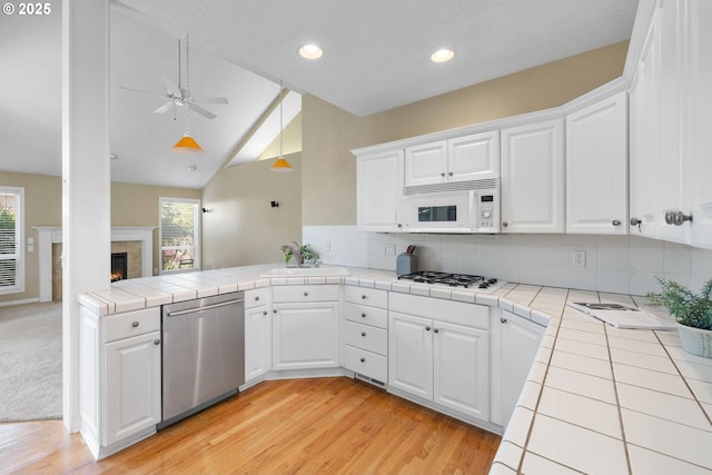 kitchen with white appliances, tile counters, a sink, a peninsula, and recessed lighting