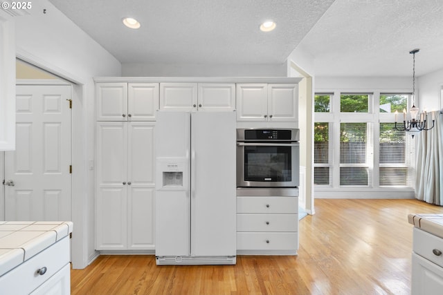 kitchen featuring white fridge with ice dispenser, oven, tile counters, a chandelier, and white cabinets