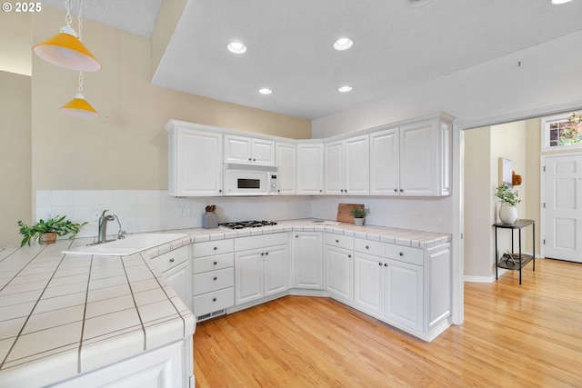 kitchen with white appliances, tile counters, recessed lighting, a sink, and white cabinets